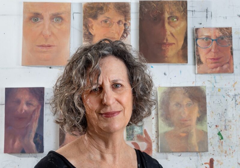 Photo of Ruth Kestenbaum Ben-Dov in her studio, with self-portraits in the background. 