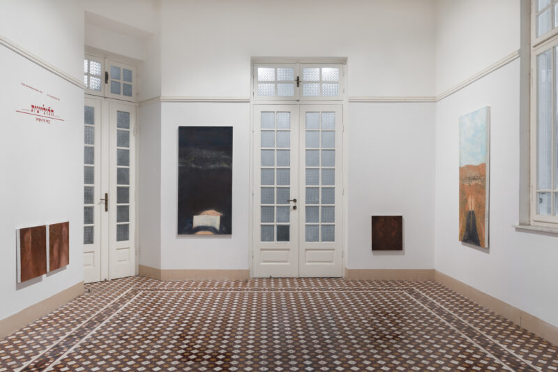 View of gallery with assorted paintings and patterned tiled floor.